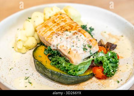 Tasty grilled salmon steak with vegetables and mashed potatoes served on light wooden table, closeup. Stock Photo