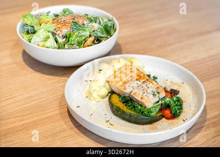 Tasty grilled salmon steak with mashed potatoes and vegetarian ceasar salad with grill steak salmon served on light wooden table. Stock Photo