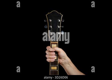 A Caucasian man's hand grips the fretboard and neck of a black electric guitar, isolated on a solid black studio background. Stock Photo