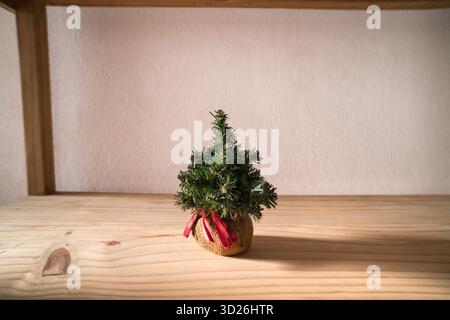 Small decorative Christmas tree with red ribbon in burlap pot on wooden table Stock Photo