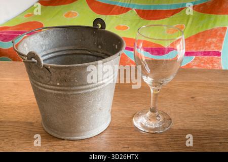 Empty wineglass and galvanized metal bucket placed on wooden surface with colorful background Stock Photo