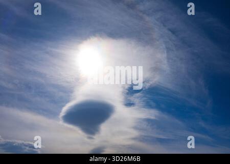 A large cloud with a sun shining through it. The sun is bright and the cloud is white Stock Photo