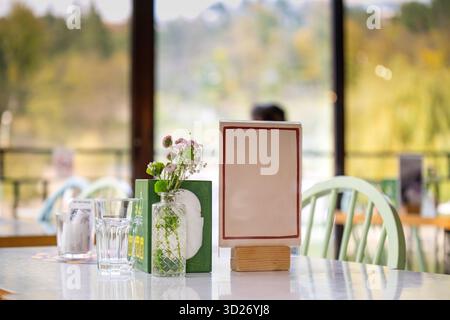 A restaurant table with a vase of flowers and a white sign. The table is set up for a meal, with a chair on each side and a few other items like cups Stock Photo
