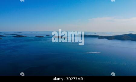 Powerful boat tracing a path of white foam across the vast, deep blue sea, its wake leading toward the tranquil islands on the horizon. Stock Photo