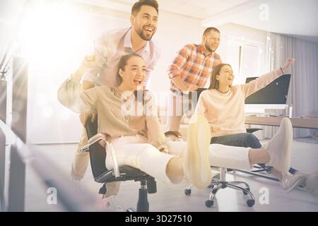 Group of happy coworkers riding chairs at workplace Stock Photo