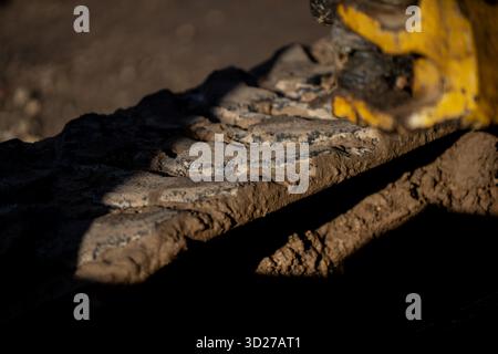 Heavy excavator steel track covered in dried mud showing traction plate details and soil adhesion on construction machinery during groundwork operatio Stock Photo
