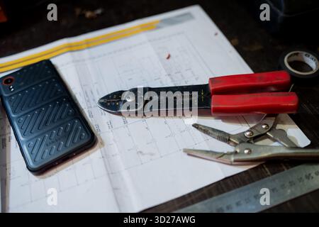 Electrician workspace with tools, phone and wiring blueprint on desk representing repair work, maintenance planning and modern engineering task prepar Stock Photo