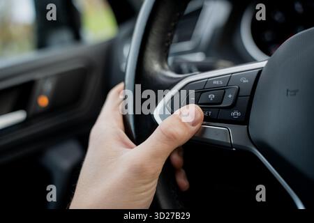 Driver hand pressing cruise control button on modern car steering wheel showing vehicle interior technology, driving comfort system and automotive con Stock Photo
