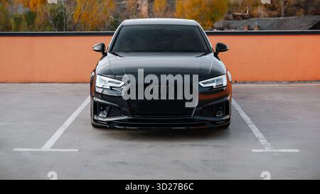 black Audi A4 at night near pastel orange fence. Wide image - front view of modern Audi sedan in parking lot on a autumn day, orange trees in the back Stock Photo
