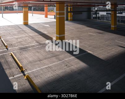 Empty parking garage, sunlight casting long shadows at the concrete floor. Top level of parking garage with yellow pillars. Stock Photo