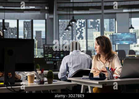Business people using laptops and computers in bright workspace, analyzing projections, metrics and reports. Team focuses on business intel, insights and targets under executive management. Stock Photo