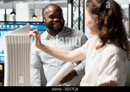 Diverse developers team reviewing architectural 3D models for zoning regulations and layout details, strategic meeting for housing project. Master plan for smart city redevelopment. Stock Photo