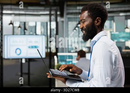 Corporate professional focused on business analytics and financial planning, working on laptop. Black male employee organizing online files and preparing key project presentation at office. Stock Photo