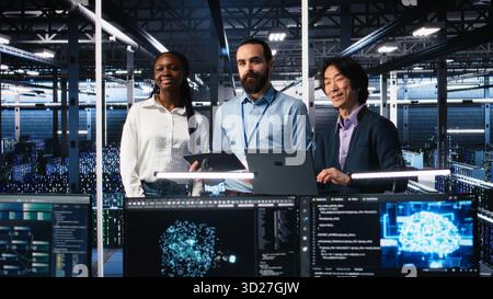 Happy data center colleagues collaborating on neural network software development. Cheerful teamworking server hub coworkers implementing machine learning technology in workplace, camera A Stock Photo