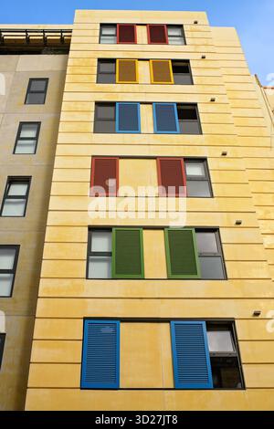 Colorful wooden shutters on narrow windows of a yellow multi-storey residential building against a blue sky. Stock Photo