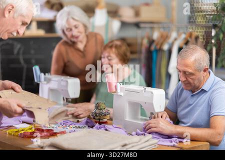 Some people communicate and discuss pattern, while others sew using sewing machine at lesson Stock Photo