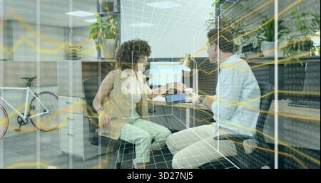 Passing stylus and tablet between colleagues in business attire at cubicle desk with data overlay Stock Photo