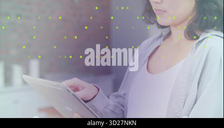Mature Asian woman wearing shirt tapping tablet in kitchen, with brick wall, copy space Stock Photo