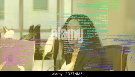 Typing coder writing code on monitor at office desk, with plant, lamp and code overlay Stock Photo