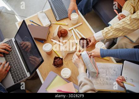 Diverse Young Adults Collaborating on Project While Sharing Snacks and Coffee Stock Photo
