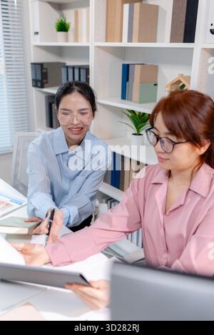 Two female colleagues discussing business reports together in a modern office environment, representing teamwork, data analysis, and collaboration in Stock Photo