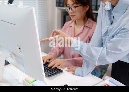 Two Asian office colleagues working together in the same department, reviewing documents and discussing project details during a team meeting, showing Stock Photo