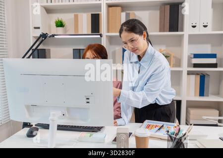 Two Asian office colleagues working together in the same department, reviewing documents and discussing project details during a team meeting, showing Stock Photo