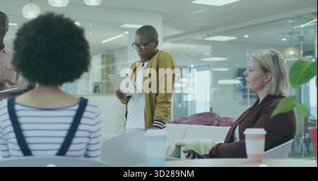 Reading from tablet African American man wearing mustard cardigan in office lounge, with papers Stock Photo