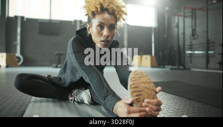 Stretching, leg and woman in gym, fitness and getting ready for workout routine, wellness and health. Flexible, athlete and person on floor for Stock Photo