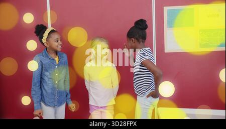 Smiling schoolgirls chatting near yellow student chair in red classroom, displaying Vision poster Stock Photo