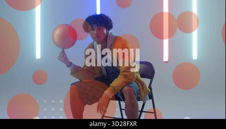 Spinning man in yellow jacket balancing sphere on finger in studio with neon lights, orange circles Stock Photo
