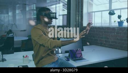 Developer wearing VR headset manipulating virtual interface in office space, with laptop smartphone Stock Photo