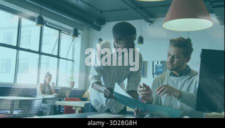 Discussing two male office workers reviewing blue folder in open-plan office, with grid windows Stock Photo