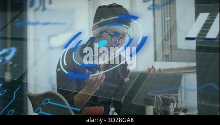 Working Asian man wearing glasses manipulating holographic overlays at office desk, with coffee mug Stock Photo