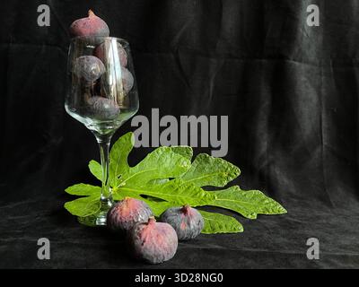 Fresh figs on a black background, served in a glass with two green fig leaves Stock Photo