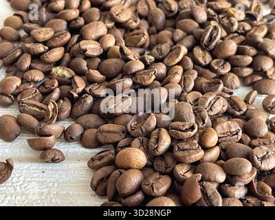 Freshly roasted coffee beans scattered on a wooden table, close-up macro shot. Stock Photo