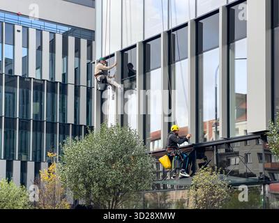 Poznan, Poland - October 10, 2025: High-angle view of dedicated workers in safety gear expertly cleaning the reflective exterior of a contemporary urb Stock Photo