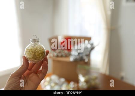 Woman holds up Christmas Ornament with decorations in background Stock Photo