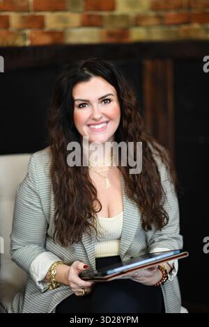 Smiling woman holding tablet in blazer with curly hair and jewel Stock Photo