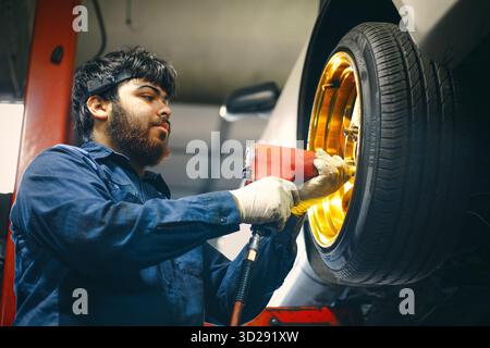 A mechanic in a blue uniform using a power tool on a golden car wheel Stock Photo