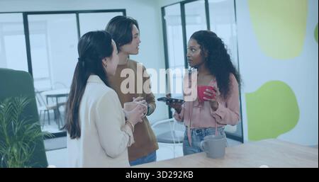 Chatting three professionals in casual wear holding coffee mugs and phone at counter in break area Stock Photo
