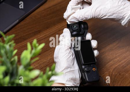 Poznan, Poland - October 16, 2025: Close-up view of person's gloved hands carefully wiping the DJI Osmo Pocket camera lens, demonstrating essential de Stock Photo