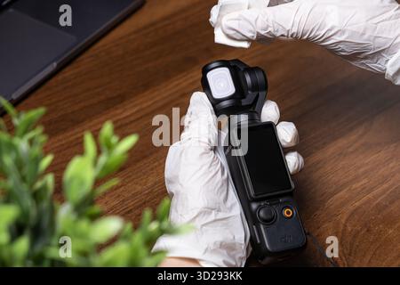 Poznan, Poland - October 16, 2025: Gloved hands diligently wiping the lens and body of a DJI Osmo Pocket 3 camera, emphasizing hygiene for sensitive d Stock Photo