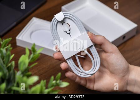 Poznan, Poland - October 16, 2025: A person's hand carefully holds a new Apple light gray braided USB-C charging cable and SIM ejector tool, ready for Stock Photo