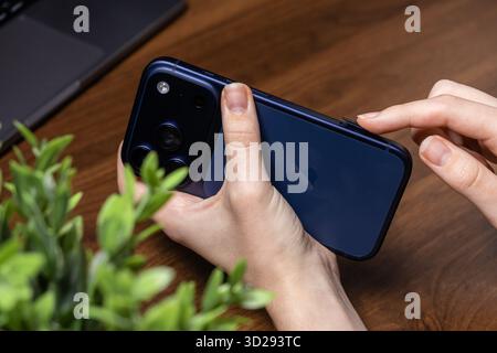 Poznan, Poland - October 16, 2025: iPhone 17 Pro, person pressing side button on the sleek dark blue device, highlighting its innovative triple camera Stock Photo