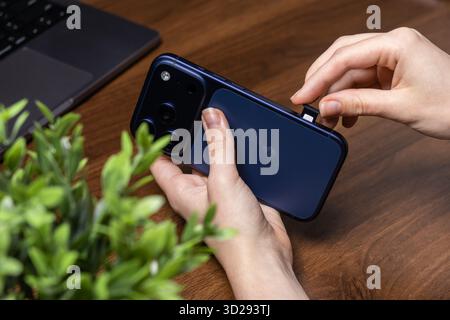 Poznan, Poland - October 16, 2025: Close-up of an iPhone 17 Pro in a hand, carefully inserting a nano SIM card into the side tray for network activati Stock Photo