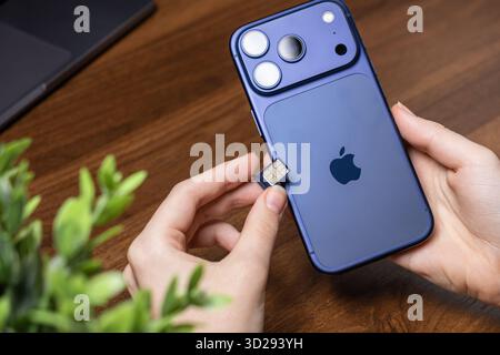Poznan, Poland - October 16, 2025: User's hands meticulously insert a nano SIM card into the purple iPhone 17 Pro, establishing crucial mobile data an Stock Photo