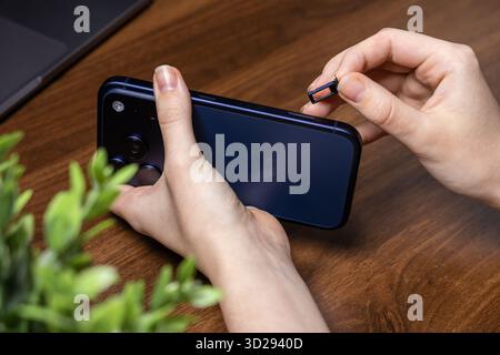 Poznan, Poland - October 16, 2025: iPhone 17 Pro, held by hands, detailing the removal of the SIM card tray, essential for mobile network activation Stock Photo