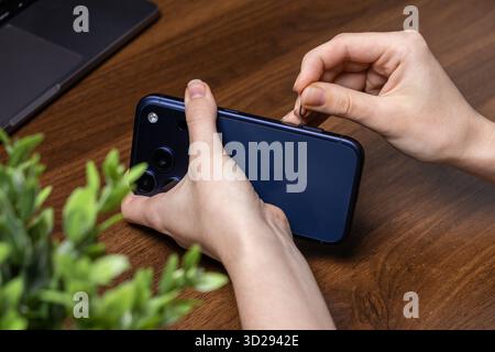 Poznan, Poland - October 16, 2025: Close-up of a new iPhone 17 Pro with hands carefully inserting a SIM card tool into the side slot, ready for device Stock Photo