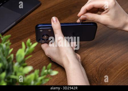 Poznan, Poland - October 16, 2025: Hands inserting a SIM tool into the dark blue iPhone 17 Pro, demonstrating device setup and essential mobile connec Stock Photo